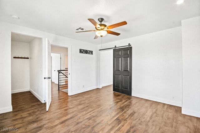 empty room featuring visible vents, a barn door, a ceiling fan, wood finished floors, and baseboards