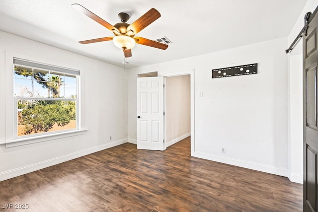 unfurnished bedroom with a barn door, visible vents, dark wood finished floors, and baseboards