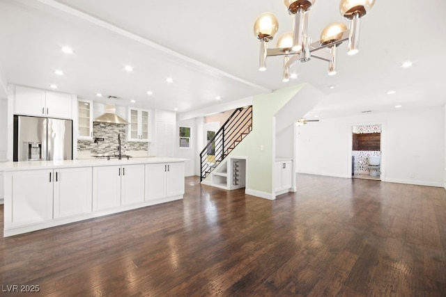 unfurnished living room featuring ceiling fan with notable chandelier, dark wood finished floors, recessed lighting, and stairs