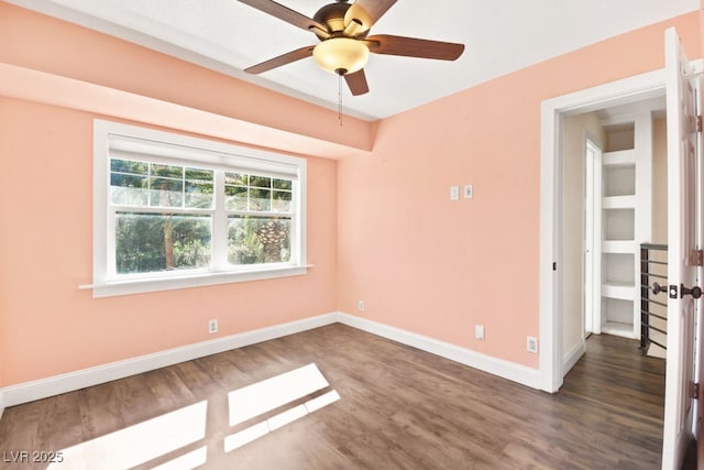 unfurnished room featuring dark wood finished floors, a ceiling fan, and baseboards