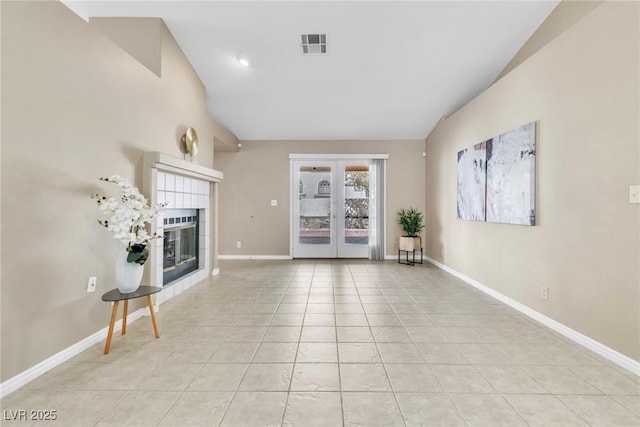 unfurnished living room with visible vents, vaulted ceiling, a tile fireplace, french doors, and light tile patterned flooring