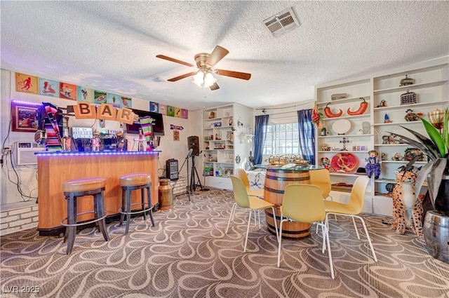 dining room with visible vents, a ceiling fan, a wall mounted air conditioner, a textured ceiling, and a bar