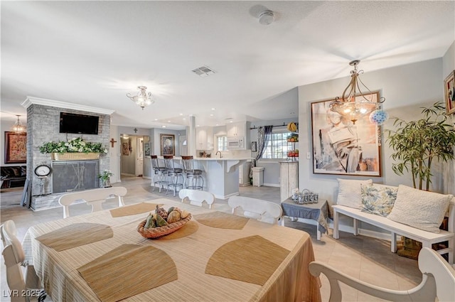 dining space with light tile patterned floors, baseboards, visible vents, a brick fireplace, and a notable chandelier