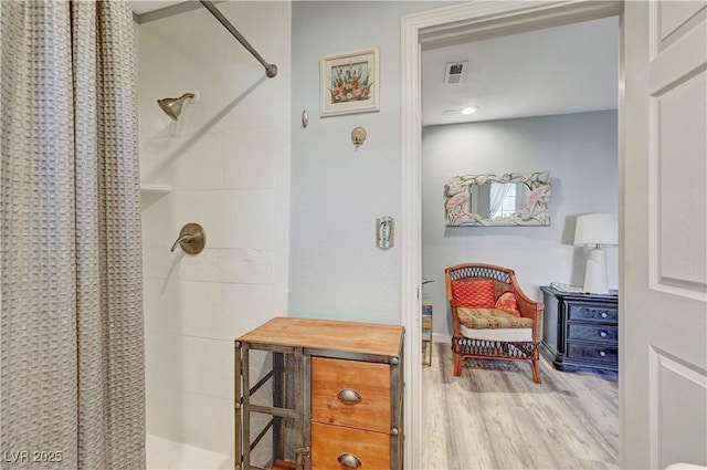 bathroom with wood finished floors, visible vents, and tiled shower