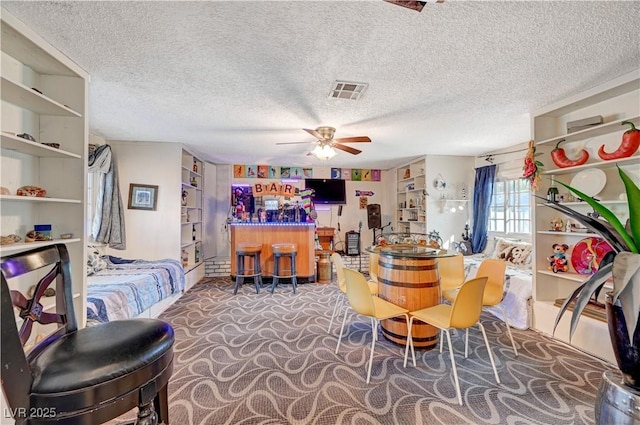 carpeted dining space featuring visible vents, a textured ceiling, a dry bar, and a ceiling fan