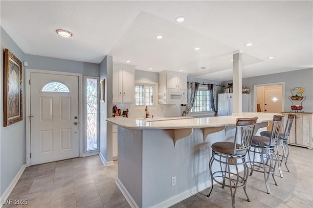 kitchen with white appliances, baseboards, light countertops, white cabinetry, and a kitchen bar