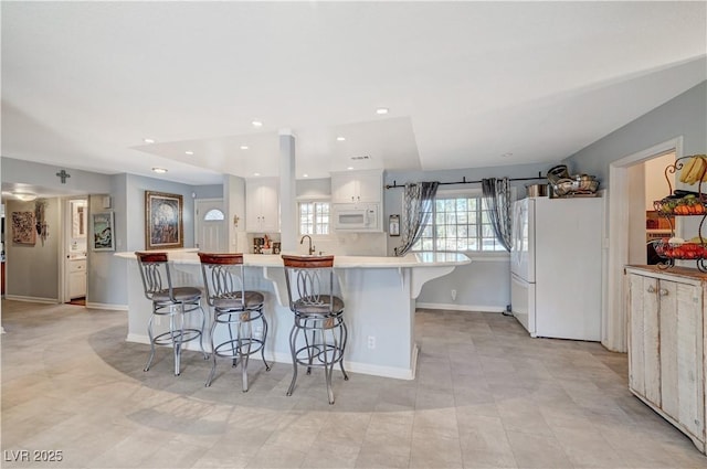 kitchen with white appliances, a sink, light countertops, white cabinets, and a kitchen bar