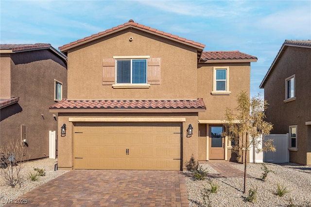 mediterranean / spanish house featuring an attached garage, a tiled roof, decorative driveway, and stucco siding