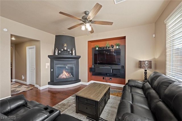 living room with a glass covered fireplace, wood finished floors, a ceiling fan, and baseboards