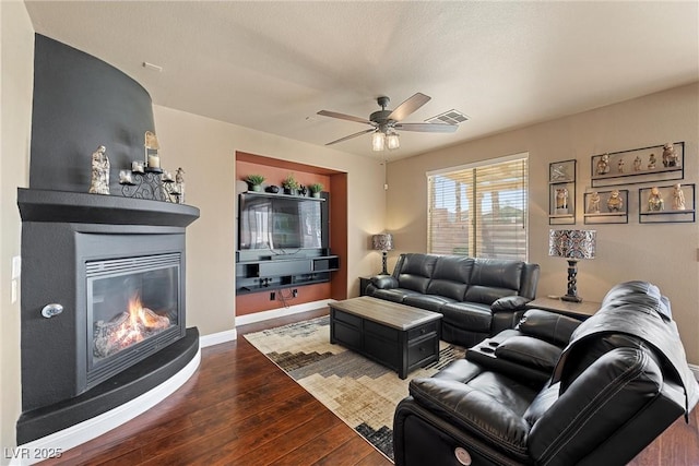 living room with baseboards, visible vents, ceiling fan, dark wood-style flooring, and a fireplace