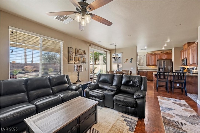 living area with a ceiling fan, visible vents, and wood finished floors