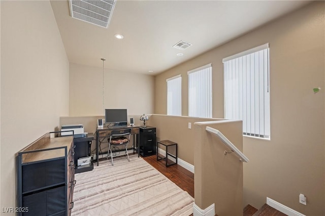 office space with baseboards, visible vents, and wood finished floors