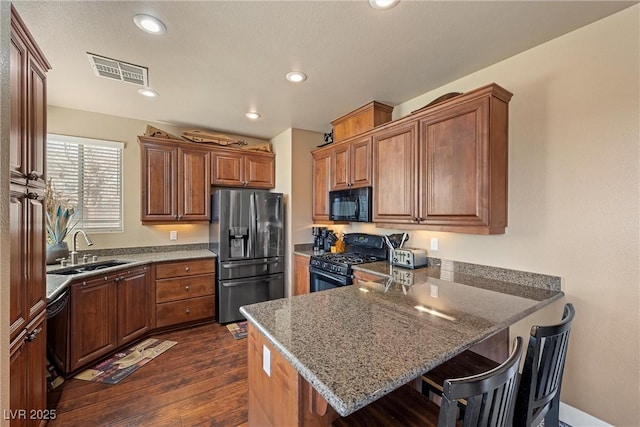 kitchen featuring a peninsula, a sink, visible vents, a kitchen breakfast bar, and black appliances