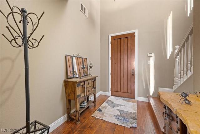 foyer featuring dark wood-type flooring, visible vents, stairway, and baseboards