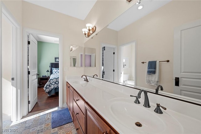 bathroom with toilet, ensuite bath, double vanity, and a sink