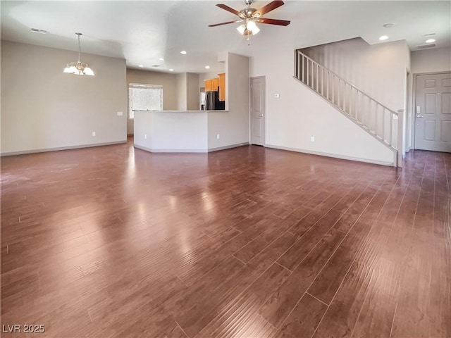 unfurnished living room with visible vents, baseboards, dark wood-style floors, stairway, and ceiling fan with notable chandelier