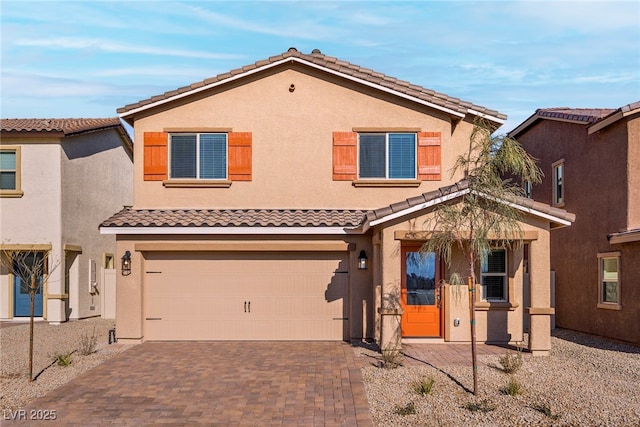 view of front facade with a garage, decorative driveway, a tile roof, and stucco siding