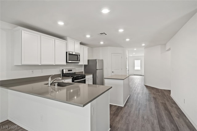 kitchen with visible vents, a kitchen island, dark wood-style flooring, stainless steel appliances, and a sink