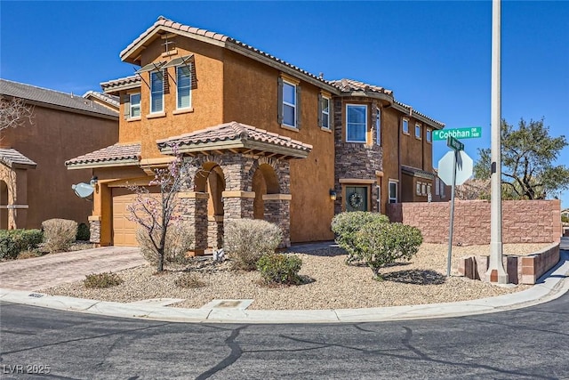 mediterranean / spanish house featuring driveway, stone siding, a tiled roof, and stucco siding