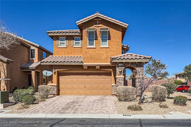 mediterranean / spanish-style house with a garage, stone siding, decorative driveway, and stucco siding