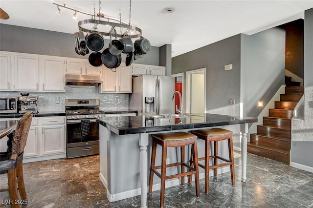 kitchen with dark countertops, marble finish floor, stainless steel appliances, under cabinet range hood, and a sink