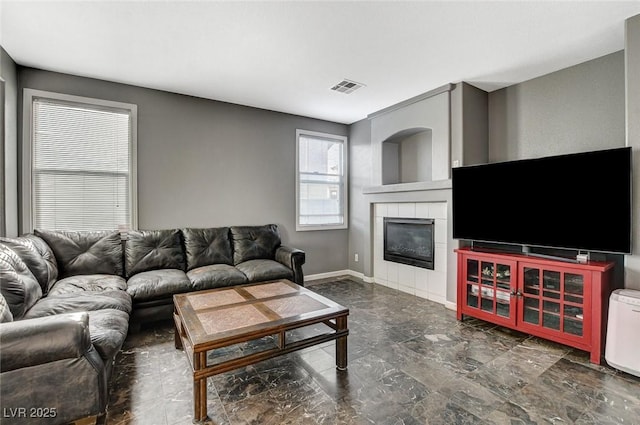 living area with a tile fireplace, visible vents, and baseboards