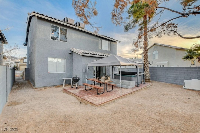 back of house featuring a fenced backyard, a hot tub, a wooden deck, and stucco siding