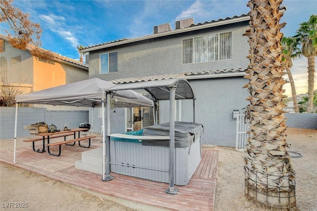 rear view of property with a tile roof, a hot tub, a wooden deck, and stucco siding