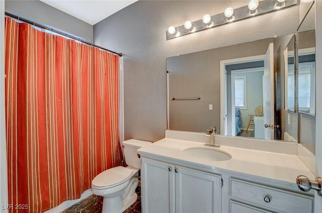 full bath featuring curtained shower, a textured wall, vanity, and toilet