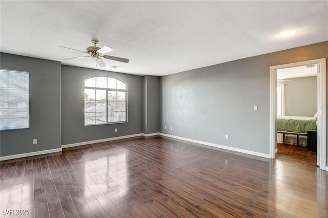 empty room featuring a ceiling fan, visible vents, baseboards, and dark wood-style flooring