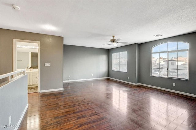 unfurnished room with dark wood-type flooring, visible vents, ceiling fan, and baseboards