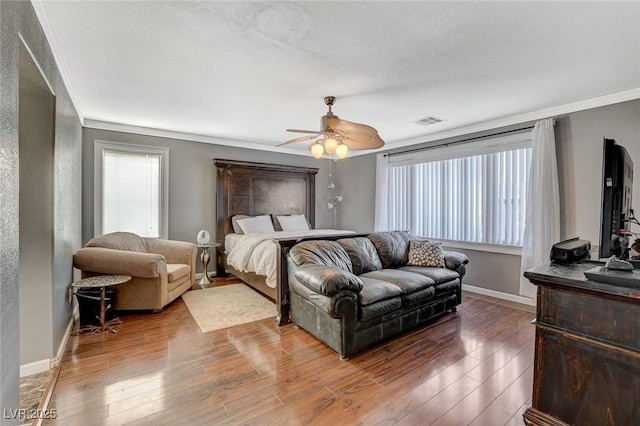 bedroom with ornamental molding, visible vents, baseboards, and wood finished floors