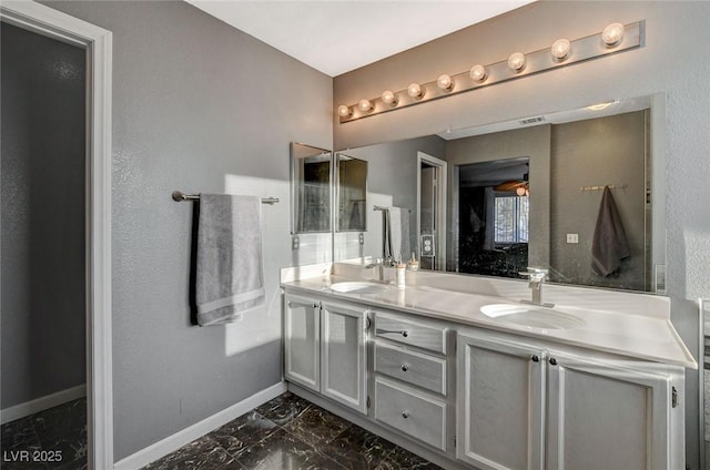 full bath with marble finish floor, a sink, baseboards, and double vanity