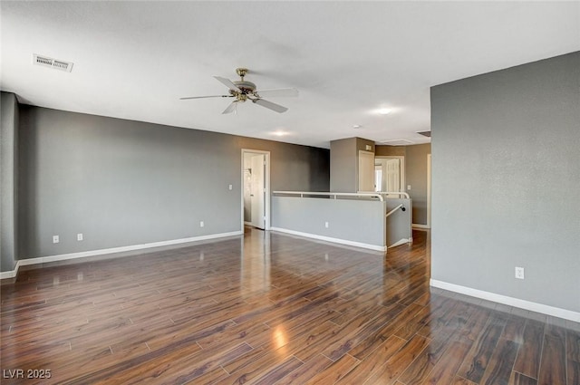 unfurnished room with dark wood-style floors, visible vents, baseboards, and a ceiling fan