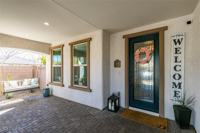 property entrance with a porch, fence, and stucco siding