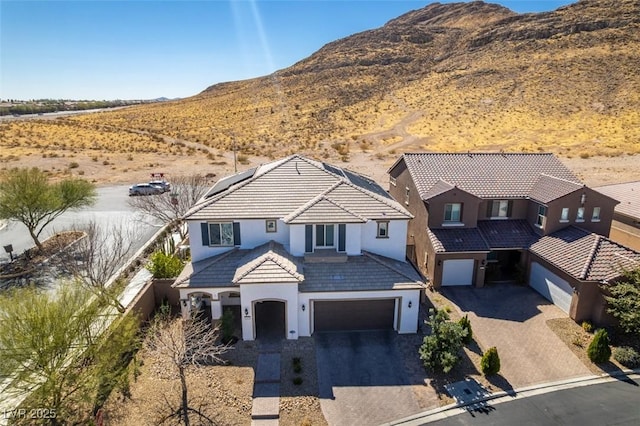 view of front of home with a mountain view, a garage, a tiled roof, driveway, and stucco siding