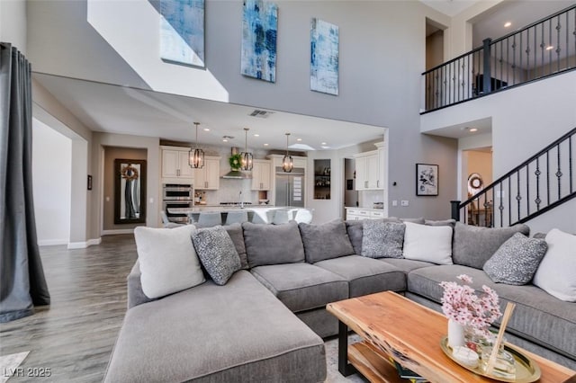 living room featuring recessed lighting, visible vents, baseboards, stairs, and light wood-style floors