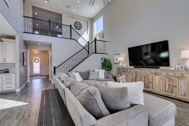 living room featuring wood finished floors, a towering ceiling, visible vents, baseboards, and stairway