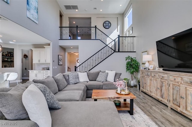 living room with light wood finished floors, baseboards, visible vents, a towering ceiling, and stairs