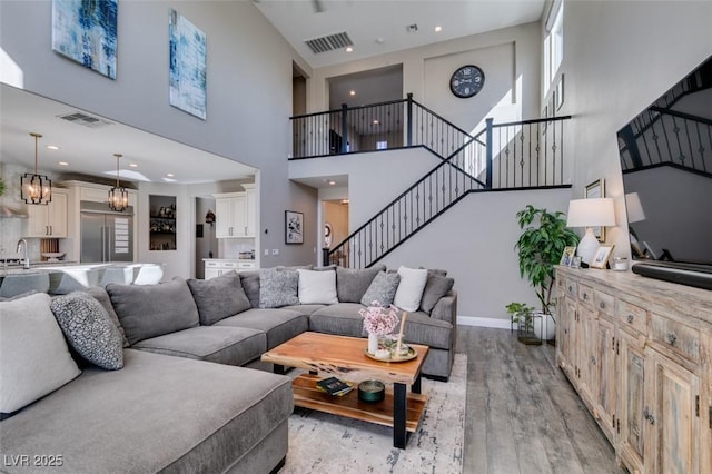 living area with stairway, light wood-type flooring, visible vents, and baseboards