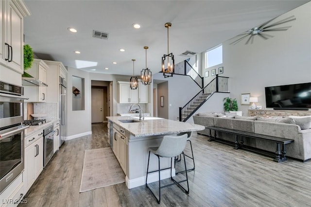 kitchen featuring a sink, visible vents, open floor plan, decorative backsplash, and a center island with sink