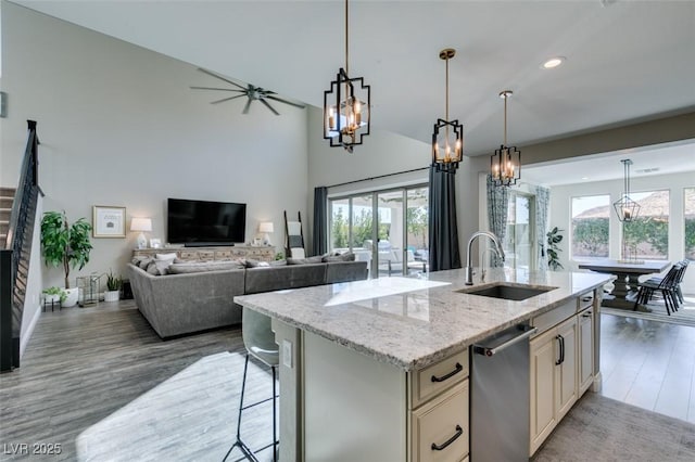 kitchen with open floor plan, wood finished floors, light stone countertops, cream cabinetry, and a sink