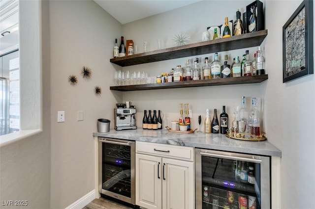 bar with a bar, light wood-style floors, wine cooler, and baseboards