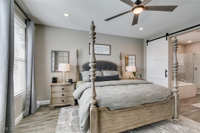 bedroom with light wood-type flooring, multiple windows, baseboards, and a barn door