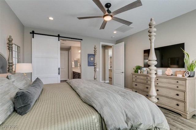 bedroom with a barn door, recessed lighting, a ceiling fan, light wood-type flooring, and ensuite bath