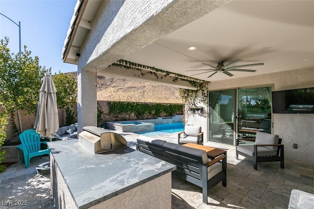 view of patio featuring a pool with connected hot tub, fence, an outdoor kitchen, and a ceiling fan