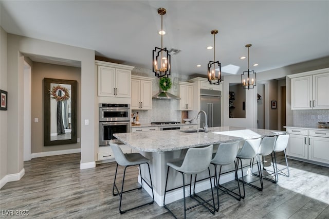 kitchen with a center island with sink, appliances with stainless steel finishes, a sink, wood finished floors, and a kitchen breakfast bar