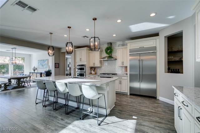 kitchen featuring dark wood finished floors, a breakfast bar area, visible vents, built in refrigerator, and wall chimney exhaust hood