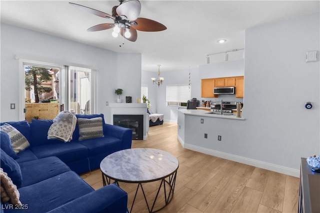 living room with light wood-type flooring, baseboards, track lighting, and ceiling fan with notable chandelier