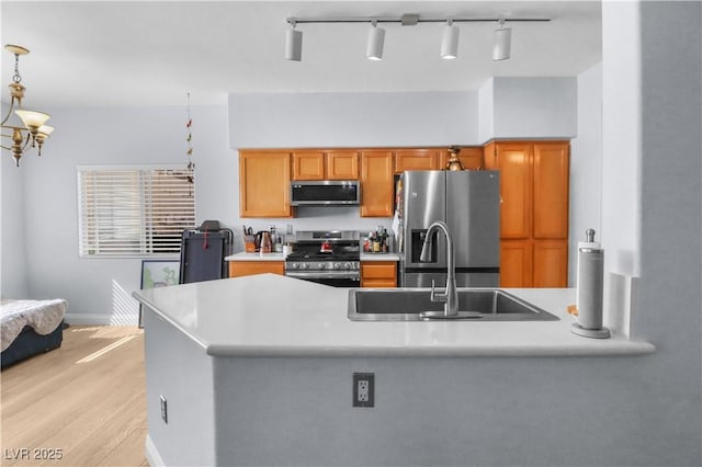 kitchen with light wood-style flooring, a sink, light countertops, appliances with stainless steel finishes, and brown cabinetry